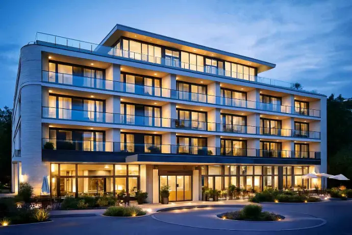 Modernes Hotelgebäude bei Abendbeleuchtung mit beleuchteten Balkonen und Eingangsbereich, beispielhaft für Einsatzbereiche der Elektrotechnik in Hall in Tirol